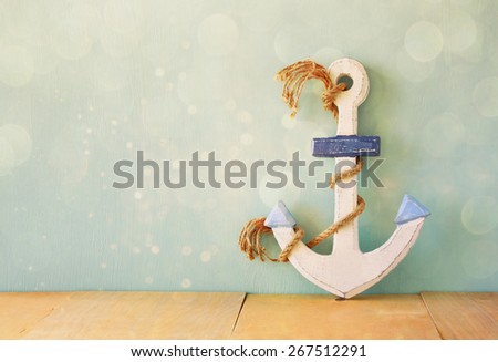 old nautical anchor on wooden table over wooden aqua background and glitter overlay

