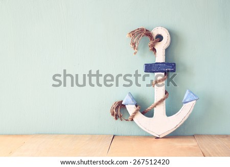 old nautical anchor on wooden table over wooden aqua background
