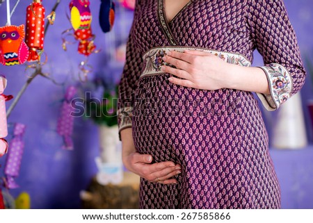 pregnant woman's belly on a colored background, arms around himself, near a tree with toys owls