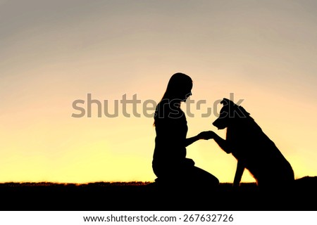 A silhouette of a young woman and her pet German Shepherd Mix Dog shaking hands at sunset.  With copy-space in sky. Royalty-Free Stock Photo #267632726