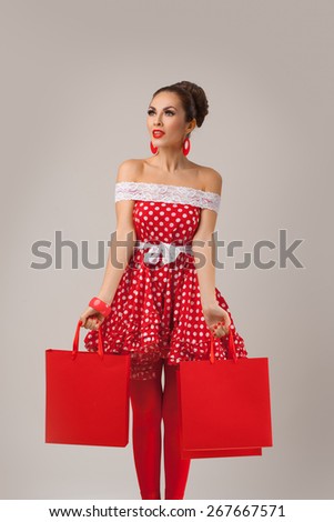 Funny portrait of a smiling cute young female model holding many shopping bags in her arms wearing red dress