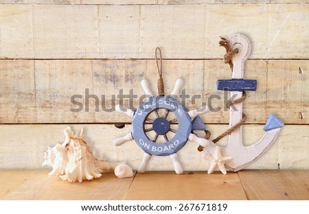 old nautical wood wheel, anchor and shells on wooden table over wooden background 