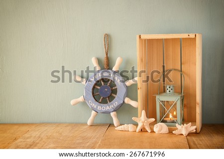 old nautical wood wheel, lantern and shells on wooden table over wooden aqua background 