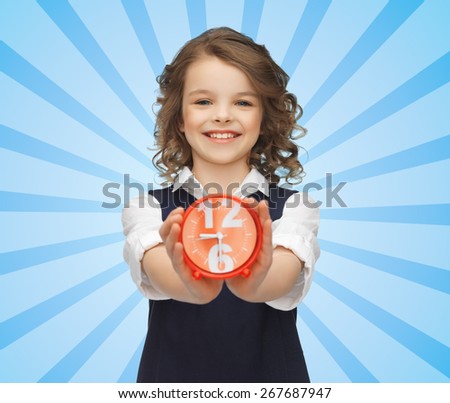 people, childhood, time and punctuality concept - happy girl with alarm clock over blue burst rays background