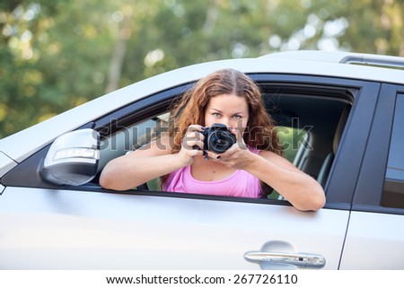 Joyful woman in pink t-shirt with photo-camera in hand taking pictures from car