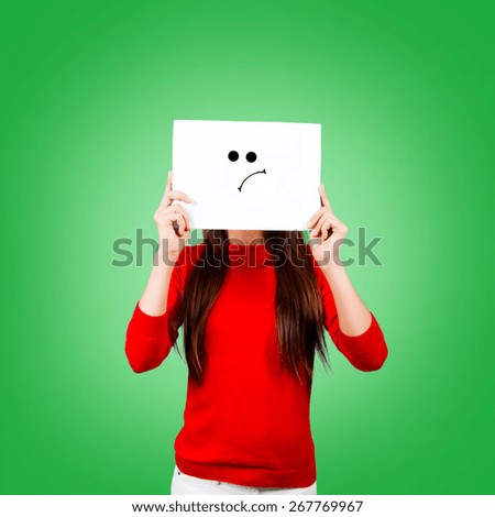 Girl holding a paper with a sad face painted

