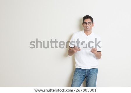 Portrait of handsome Indian guy using tablet pc, standing on plain background with shadow, copy space at side.