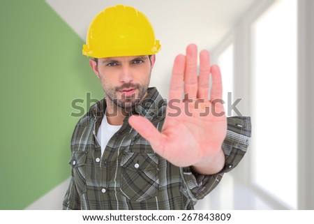 Confident manual worker gesturing stop sign against modern white and green room with window