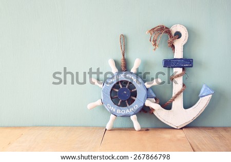 old nautical wood wheel and anchor on wooden table over wooden aqua background 