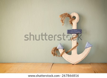 old nautical anchor on wooden table over wooden aqua background 