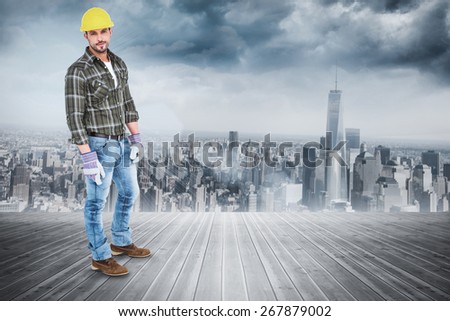 Full length portrait of confident handyman against room with large window looking on city