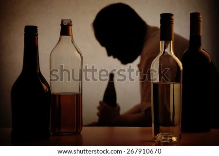 silhouette of a person drinking behind bottles of alcohol with added filter                             Royalty-Free Stock Photo #267910670