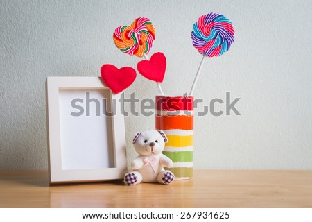 White photo frame, Lollipop and teddy bear on wooden table over wall background, vintage style