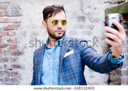 Handsome man with glasses ina suit, against old vintage wall, outdoors. taking a selfie