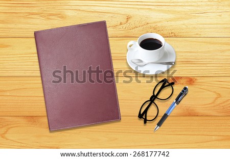 Notebook with office supplies with pen with glasses and cup of coffee on wooden table.