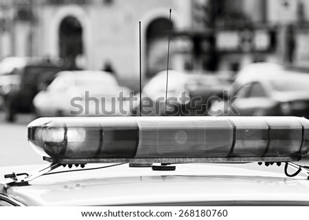 the blinking police alarm system of the official car and photographed on an indistinct background of city streets and motor transport in monochrome tones