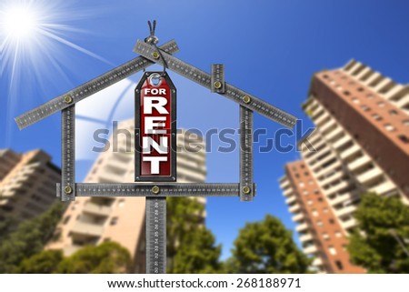House For Rent Sign - Metallic Meter. Grey metallic meter ruler in the shape of house and label with text for rent. For rent real estate sign with tall and blurred buildings in the background