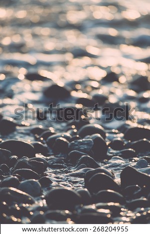 sun reflections on Stones on the beach and sea water in sunset light - retro vintage film effect