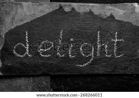 The word DELIGHT written with chalk on black stone.