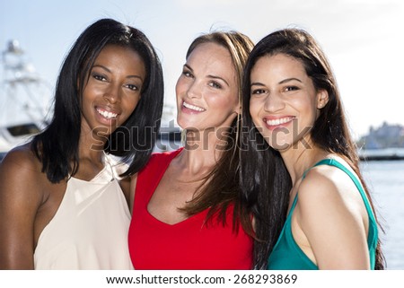 Three women posing in marina harbor, yachts on background. 