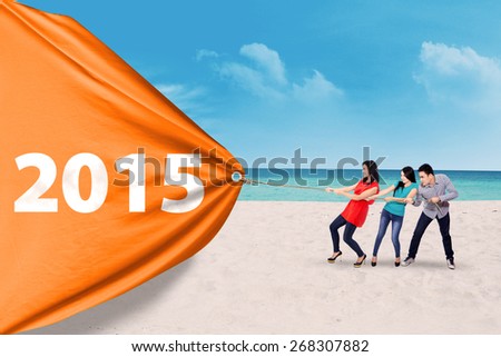 Attractive young people pulling a big banner with number 2015 on the beach