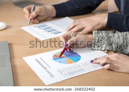 Working on charts. Hands of business people male and female working on printer paper charts analyzing data and pointing smart casual dress code wood texture desk cropped laptop from above view
