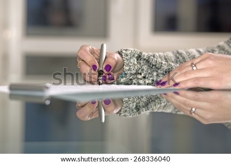 Lady signs formal document. Close up of female hands with one hand holding vintage fountain pen and another - keeping piece of paper on the glass table with strong reflections