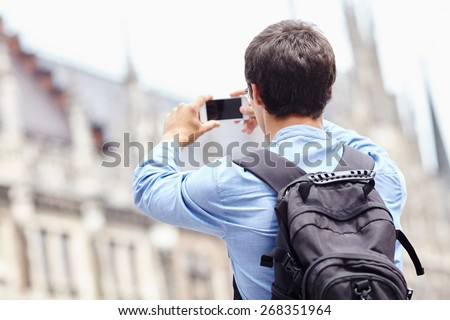 Young man with backpack taking picture with smartphone on city center during vacation
