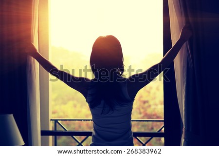 young woman opening curtains in a bedroom Royalty-Free Stock Photo #268383962