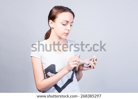 Half Body Shot of a Serious Young Woman in Casual Wear Holding a Makeup Against a Gray Background