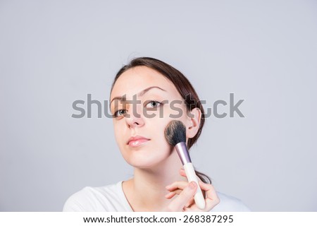 Close up Pretty Young Woman Applying Makeup on her Cheek Using a Brush While Looking at the Camera.