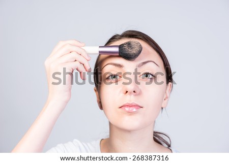 Close up Serious Young Woman Applying Foundation Makeup on Forehead While Looking at the Camera on a White Background.