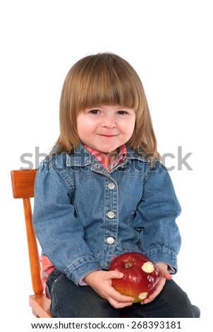 Two years old girl in a blue jacket trying to eat an apple