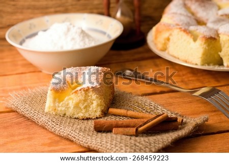 Horizontal photo of Portion of curd cake together with cinnamon on jute cloth, fork and bowl with powder sugar plus other portions in background