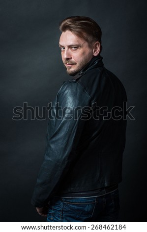 brutal bearded man in black leather jacket looks looks suspiciously to the camera