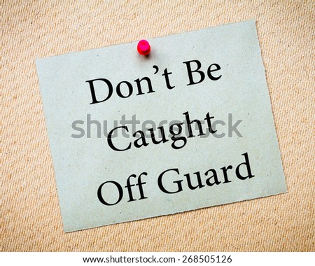 DON'T BE CAUGHT OFF GUARD Message. Recycled paper note pinned on cork board. Concept Image