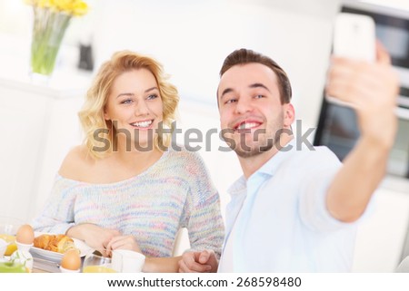 A picture of a young couple eating breakfast in the kitchen and taking selfie