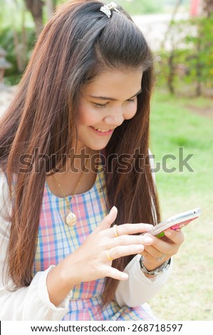 Modern teenager girl using a smart phone in a park with a green background