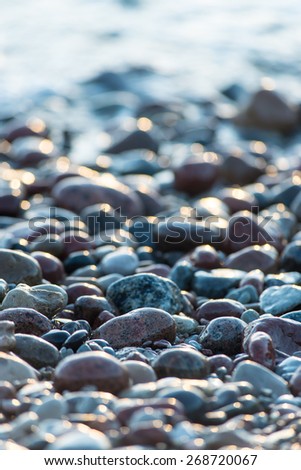 sun reflections on Stones on the beach and sea water in sunset light