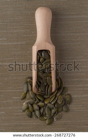 Top view of wooden scoop with pumpkin seeds against green vinyl background.