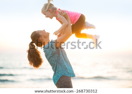 Mother throwing baby up on beach in the evening Royalty-Free Stock Photo #268730312