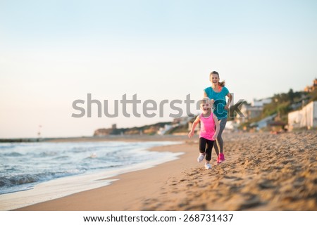 Healthy mother and baby girl running on beach in the evening