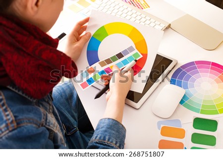 young woman artist in jeans jacket with color samples drawing something on graphic tablet at the office