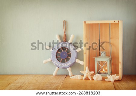 old nautical wood wheel, anchor and shells on wooden table over wooden background
