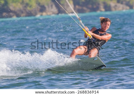 A young woman kite-surfer rides in blue sea