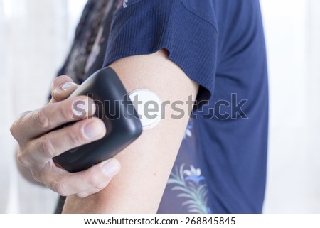 closeup of a hand of a young woman is scanning the sensor of the glucose monitoring system at the back of her arm with the reader - focus on the sensor Royalty-Free Stock Photo #268845845