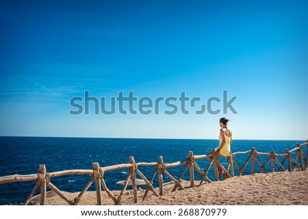 beautiful woman sitting on a wooden fence and looking at the sea.