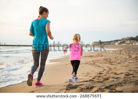 Healthy mother and baby girl running on beach. rear view Royalty-Free Stock Photo #268879691