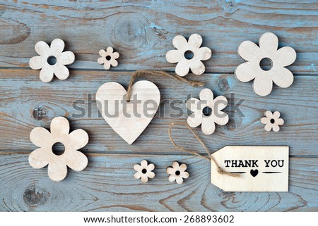 Blue grey wooden background with label with thank you text and wooden flowers and heart