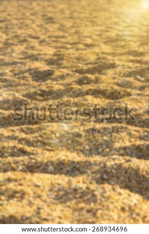 Blurred background image of sea sand and sun. Blurred picture with: partly visible texture of small stones and sand seashore lit by light rays of the evening sun. Beach, seashore. Support of the text.